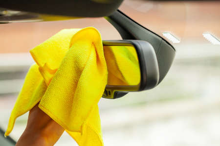 Hand with yellow microfiber cloth polishing car