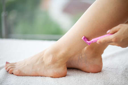 Young woman removing hair on legs with razor at bathroomの写真素材