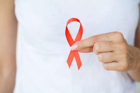 Woman hand holding red ribbon HIV, world AIDS day awareness ribbon.