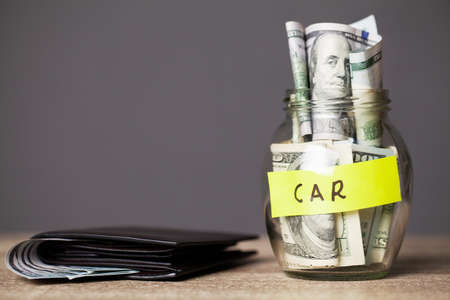 Dollar bills in glass jar and text car on wooden table