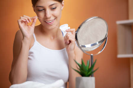 Portrait of beautiful woman cleaning teeth with dental flossの写真素材