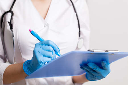Doctor writes down patient medical history with pen on cardの写真素材