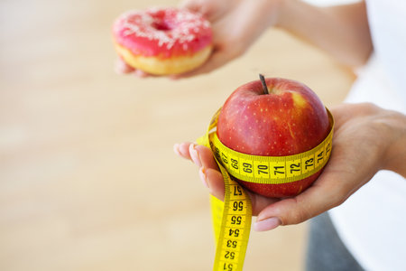 Young attractive girl is making choice between healthy and harmful food holding apple and a burger in her hands.の写真素材