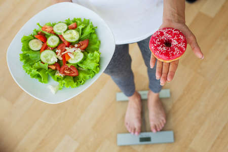 Dieting concept, beautiful young woman choosing between healthy food and junk food.の写真素材