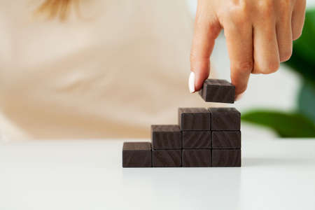 Hand putting wood cube on top of wood block stacking as step stairの写真素材