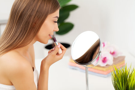 Beautiful woman fresh healthy skin looking on mirror makes makeupの写真素材