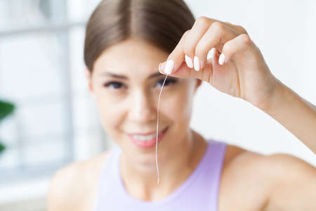 Portrait of beautiful woman cleaning teeth with dental floss