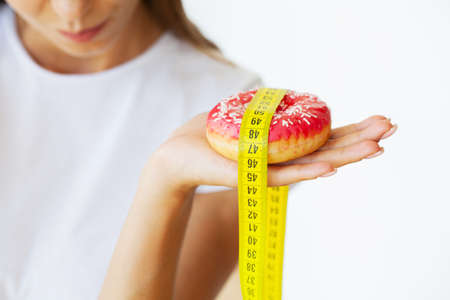 Young woman standing on scales and holding a donut.の写真素材