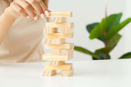 Womans hand makes wooden cubes on a white tableの写真素材