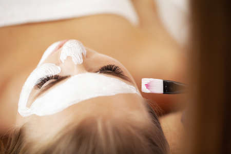 Young beautiful girl receiving white facial mask in spa beauty salonの写真素材