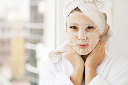 Beautiful Woman Applying Paper Sheet Mask On Her Face Whiteの写真素材