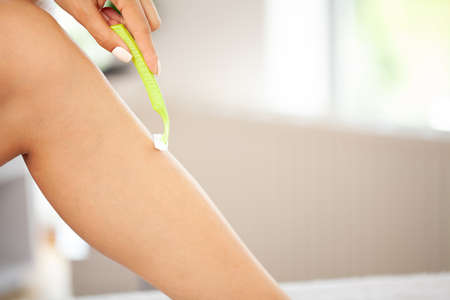 Young woman shaving legs with a razor blade in the bathroom