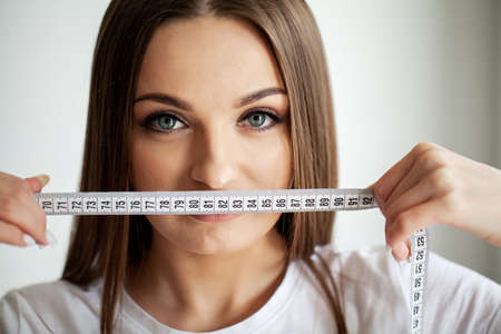 Closeup of beautiful young woman with measure tape near her faceの写真素材