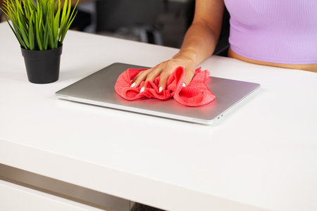 A cleaner cleans the office by wiping dust from a laptop