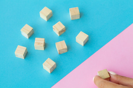 Wooden blocks with a human hand placing one cube at the top on blue background.の写真素材