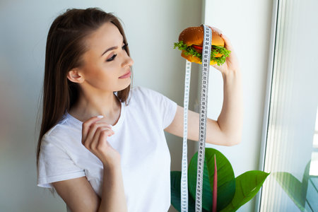 Woman with burger and measuring tape while dietingの写真素材
