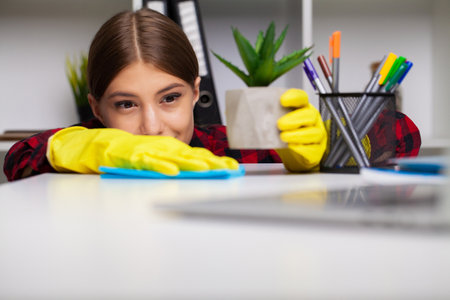 Cleaner cleans office in the yellow gloves wipes the dust off the office deskの写真素材