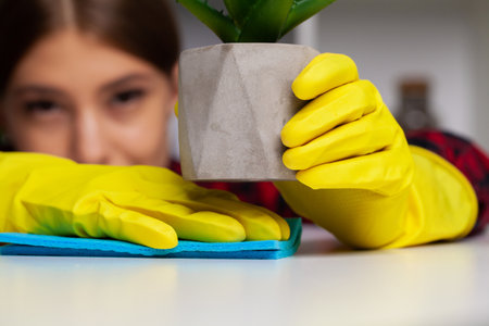 Woman cleans office in the yellow gloves wipes the dust off the office desk