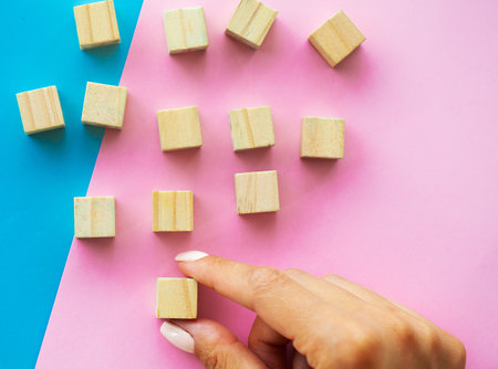 Female hand arranging empty wood block and copy space on blue and pink background