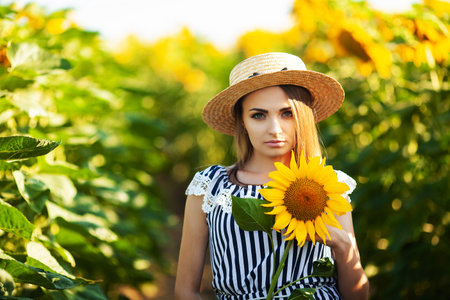 Beautiful blonde woman in the flowers field on sunset in straw hatの写真素材