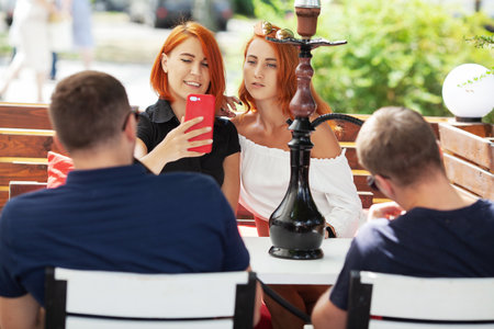 Two young cute girls smoke hookah in a cafe on a summer day on the terrace