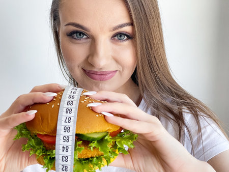 Woman with burger and measuring tape while dietingの写真素材