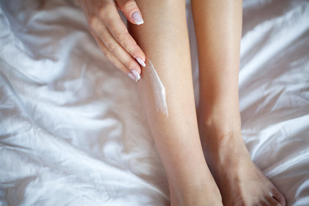 Young woman applying body lotion on legs