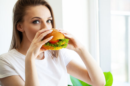 Young woman eats a fatty burger, weight loss concept.の写真素材