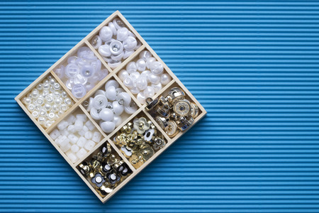 Clothes buttons in wooden box on blue cardboard background. Closeup photo shot from topの写真素材
