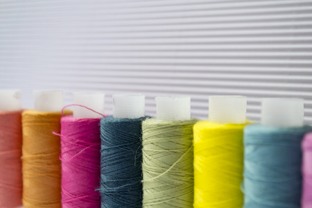 Various colored threads with clothes buttons on white cardboard background.