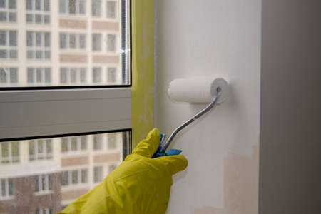 painting the window slope with a roller. worker's hand in a yellow glove. White water-based paintの写真素材
