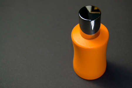 orange perfume bottle with a shiny cap on a black background. side view of the bottle