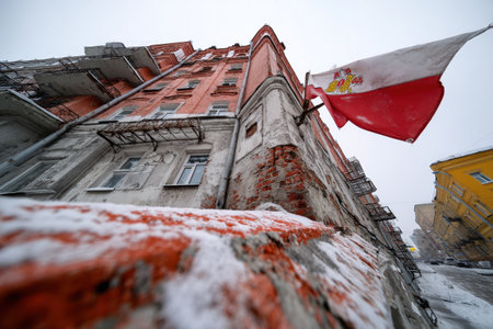 Snow covers the ground as an aged building shows wear, with a flag waving in the cold air.の素材