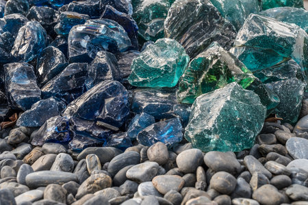 A pile of blue and green glass stones on a pebble beach