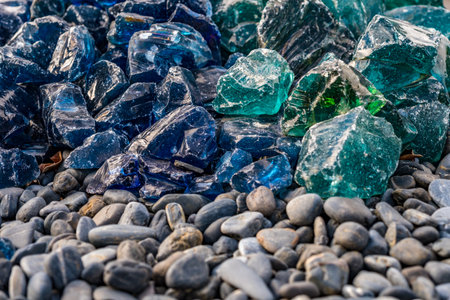 Blue and green broken glass pieces on pebble beach, backgroundの写真素材