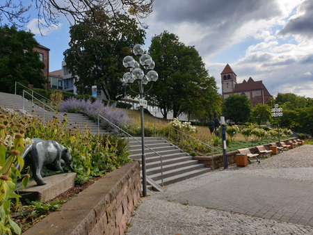 A city park with blooming shrubs along a staircase. In the background stands a church with a clock tower. The park includes benches and street lamps.の写真素材
