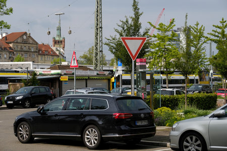 A city street with parked cars, traffic signs, and roadside greenery. In the background, buildings, construction cranes, and public transportation complete the urban scene.の写真素材