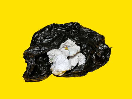 Black polithin and paper waste isolated on yellow background. Plastic and paper waste concept for recycling.の写真素材