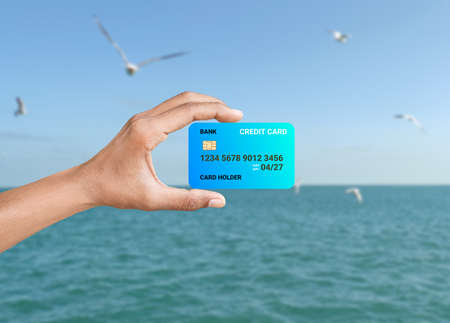hand hold blue credit card isolated on blur ocean background. concept for vacation on credit card.