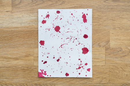 Piece of paper spotted with red ink in a wooden backgroundの写真素材