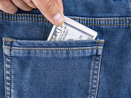 A hand takes money out of the back pocket of jeans. Theft. Robbery. Place for text.