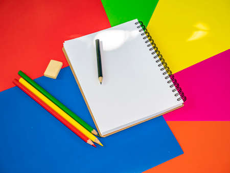 Colored pencils for drawing on the table. Multicolored background. Sharpened pencil. School drawing lesson. Eraser. Place for your text. Template. Background image. Sheets of colored paper. Notebook.の写真素材