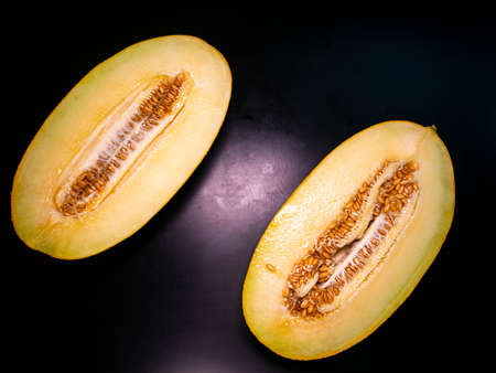 Yellow melon cut with a knife on a black background. Food photo. Melon culture. Agriculture. Place for your text. Black background. Background image. Shchablon. Poster. Vegetarian food.の写真素材