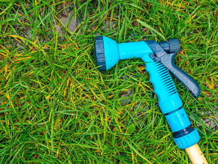 Blue gun spray water on the hose for watering the lawn. Blue spray gun for watering green grass. Irrigation of the garden with a garden hose. Gardening. Farming. Agriculture. Place for your text.の写真素材