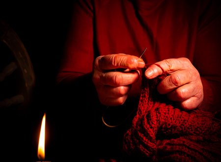 Hand knitting with woolen thread by candlelight. Knitting needles. Woolen thread. Old man's hands. Handwork. Weave warm clothes. Manual creativity. Self made. The flame of a wax candle.の写真素材