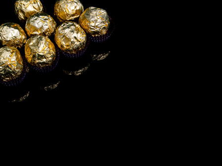 Round chocolate candies in a golden wrapper on a black background. Round candies. Golden color. A holiday gift. Birthday. Food photo. Sweet food. Happy birthday. Background image. Chocolate.の写真素材
