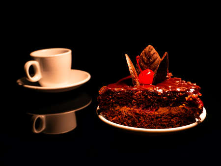 Chocolate cake with cherries and a cup of coffee on a black background.の写真素材