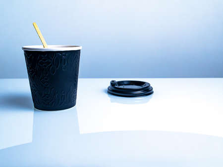 Black disposable paper cup with plastic lid for coffee drinks. Disposable paper cup. Coffee. Street Cafe. Dishes for hot drinks. Cardboard dishes. White kitchen table. Background image.の写真素材