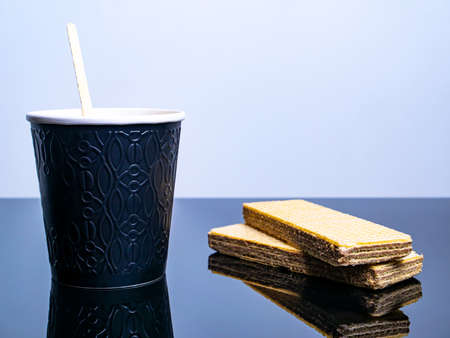 Black paper disposable cup for coffee drinks and waffle cookies on the table. Coffee drink Waffle dessert. Street Cafe. Paper cup. Disposable tableware. Dishes for hot drinks. Tea. Table.の写真素材