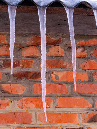 Icicles of frozen water on the roof of a house with a brick wall. Snow melting. Winter. Spring drops. Ice icicle. Frozen water. Brick wall. Frosty frost. Winter season. Roof of the house.の写真素材